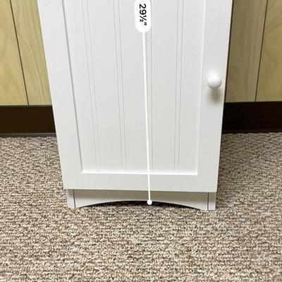 Sale Photo Thumbnail #405: White wooden cabinet featuring an open upper shelf compartment and a lower section enclosed by a paneled door with a round knob. The cabinet measures 10 inches deep, 12.5 inches wide, and 29.5 inches tall. It includes two shelves behind the door. The over