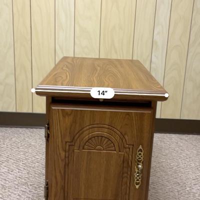 Sale Photo Thumbnail #468: Wooden side cabinet measuring 23 inches in width, 14 inches in depth, and 20 inches in height. It features a hinged door with decorative details and metal hardware, revealing an interior storage compartment. The cabinet is constructed in a warm-toned wood