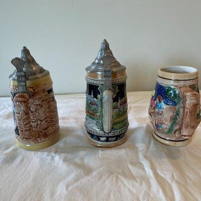 Sale Photo Thumbnail #552: Three decorative German beer steins with intricate relief designs and vibrant hand-painted scenes. Two steins feature lidded pewter tops with classical motifs, while one is lidless. One stein is marked with the GERZ brand on the base, denoting quality cra