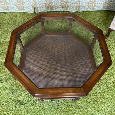 Sale Photo Thumbnail #567: Octagonal coffee table featuring a wooden frame and a glass top. The table includes an inset caned shelf beneath the glass surface and is supported by multiple decorative turned legs. Dimensions are approximately 31.5 inches in height and 3 feet 1 inch in