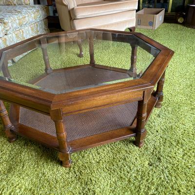 Sale Photo Thumbnail #566: Octagonal coffee table featuring a wooden frame and a glass top. The table includes an inset caned shelf beneath the glass surface and is supported by multiple decorative turned legs. Dimensions are approximately 31.5 inches in height and 3 feet 1 inch in