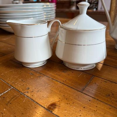 Sale Photo Thumbnail #110: Timeless and refined, this 1995 “Classic Elegance” fine china set by The Cellar includes dinner plates, salad plates, bowls, cups, a teapot, creamer, sugar bowl, and serving pieces. White with a thin gold rim, perfect for formal dining or holiday gath