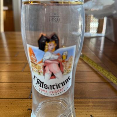 Sale Photo Thumbnail #162: Humorous collectible beer glass with vintage-style art and gold rim. Features “L’Alsacienne sans culotte” design—quirky and eye-catching.