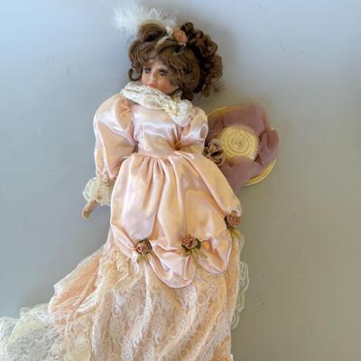 Sale Photo Thumbnail #176: Elegant vintage-style porcelain doll in a peach satin and lace gown, detailed with rose accents and a feathered hairpiece. Includes matching hat.