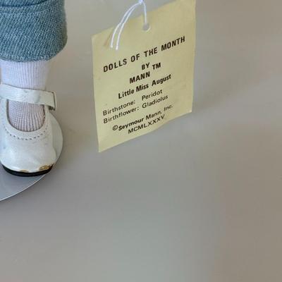 Sale Photo Thumbnail #179: Porcelain collector's doll representing July. Dressed in denim overalls and gingham blouse, holding a picnic basket. Comes with original tag.