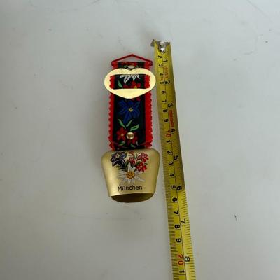 Sale Photo Thumbnail #312: Decorative brass bell with alpine floral design and "München" (Munich) label. Includes red-and-black fabric hanger.