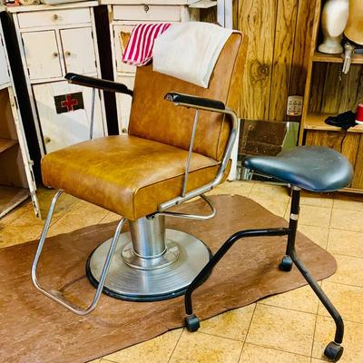 LOT 86: Mid - Century Adjustable Barber’s Chair with Barber Capes and a Three Leg Roll About Stool