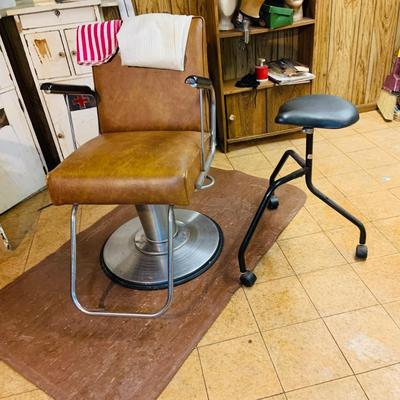 LOT 86: Mid - Century Adjustable Barber’s Chair with Barber Capes and a Three Leg Roll About Stool