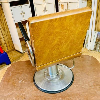 LOT 86: Mid - Century Adjustable Barber’s Chair with Barber Capes and a Three Leg Roll About Stool