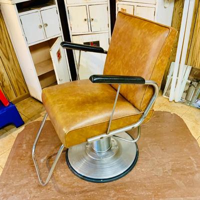 LOT 86: Mid - Century Adjustable Barber’s Chair with Barber Capes and a Three Leg Roll About Stool