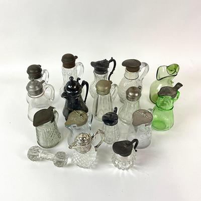 Sale Photo Thumbnail #1305: Total of 17 items
Two green glass pitchers, 15 clear glass pitchers
Only one has no top, one has broken top hinge
Tallest: 7" high
Shortest: 4" high