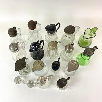 Sale Photo Thumbnail #1308: Total of 17 items
Two green glass pitchers, 15 clear glass pitchers
Only one has no top, one has broken top hinge
Tallest: 7" high
Shortest: 4" high