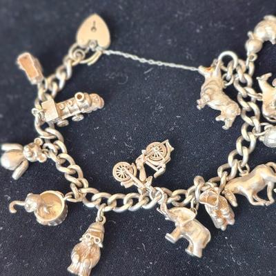 Sale Photo Thumbnail #118: Heavy charm bracelet, marked silver on the heart shape latch.  
Tower of London, locomotive, bear with articulated arms, trashcan with articulated mouse, 
Paddington Bear with marks, bicycle, elephant, soldier with tricorn hat, horse, rabbits, horse with 