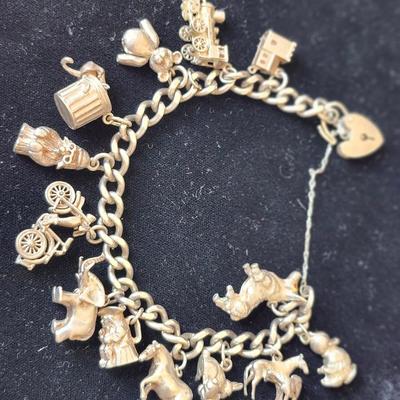 Sale Photo Thumbnail #119: Heavy charm bracelet, marked silver on the heart shape latch.  
Tower of London, locomotive, bear with articulated arms, trashcan with articulated mouse, 
Paddington Bear with marks, bicycle, elephant, soldier with tricorn hat, horse, rabbits, horse with 
