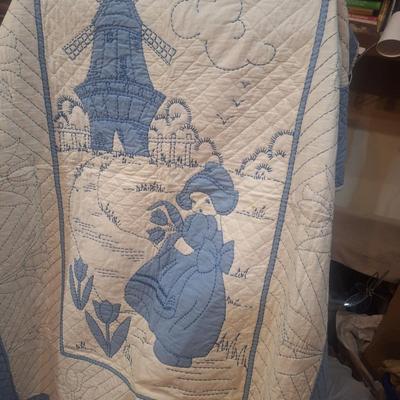 Sale Photo Thumbnail #623: looks to be hand embroidered.  Dutch girl and windwmill it is approx 4 ft wide (did not actually measure it but he rack it's hanging from is a 4ft rack that is 6ft tall, the quilt is not touching the floor but it does span end to end on the rack.