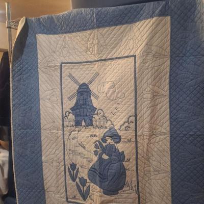 Sale Photo Thumbnail #624: looks to be hand embroidered.  Dutch girl and windwmill it is approx 4 ft wide (did not actually measure it but he rack it's hanging from is a 4ft rack that is 6ft tall, the quilt is not touching the floor but it does span end to end on the rack.