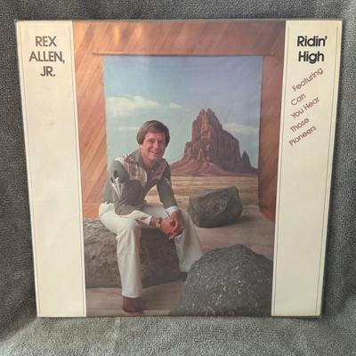 Sale Photo Thumbnail #390: "Ridin' High" by Rex Allen, Jr., a vinyl LP released by Warner Bros. in 1976. 
Key details about the album:
Artist: Rex Allen, Jr.
Album Title: Ridin' High
Release Year: 1976
Record Label: Warner Bros. Records
Format: Vinyl LP
Featured Track: "Can You Hea