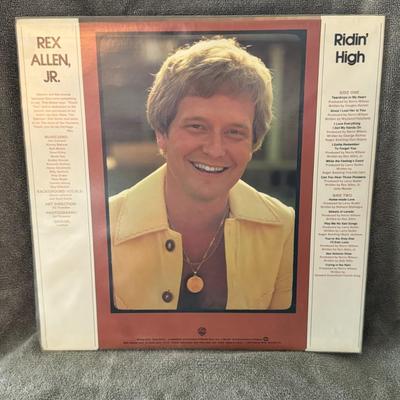 Sale Photo Thumbnail #391: "Ridin' High" by Rex Allen, Jr., a vinyl LP released by Warner Bros. in 1976. 
Key details about the album:
Artist: Rex Allen, Jr.
Album Title: Ridin' High
Release Year: 1976
Record Label: Warner Bros. Records
Format: Vinyl LP
Featured Track: "Can You Hea