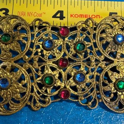 Vintage brooch featuring an ornate gold-toned filigree design adorned with colorful rhinestones,