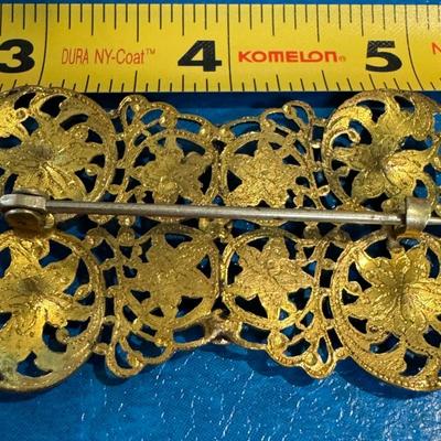 Vintage brooch featuring an ornate gold-toned filigree design adorned with colorful rhinestones,