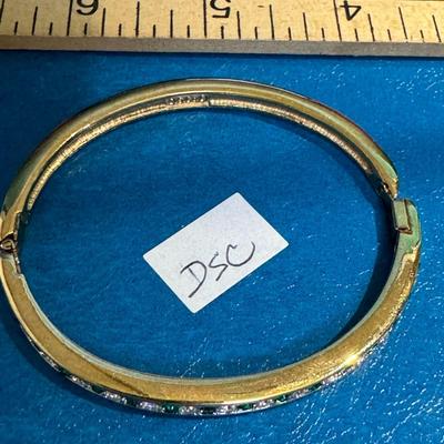 Gold-tone hinged bangle bracelet adorned with channel-set emeralds and clear rhinestones,