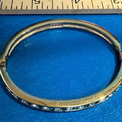 Gold-tone hinged bangle bracelet adorned with channel-set emeralds and clear rhinestones,