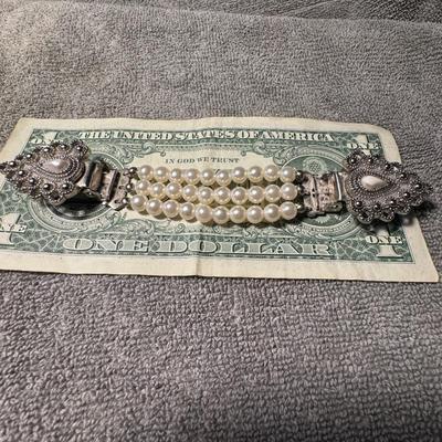 Triple-strand pearl sweater clip featuring a distinctive, ornate silver-toned clasp,