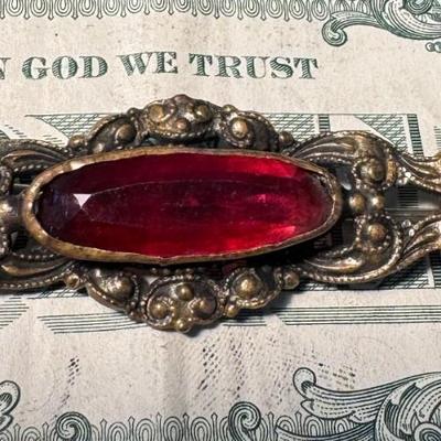 Brooch featuring a prominent red gemstone, likely a large red glass or rhinestone,