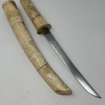 Sale Photo Thumbnail #72: 9 3/4” blade and 20” overall
19th century Japanese Meiji Era tanto samurai knife with a straight single-edged blade. It has ivory or ox bone hand carved mounts depicting traditional scenes. The sheath is chipped at the bottom.