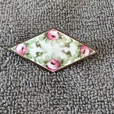 Rhombus-shaped pin featuring a hand-painted or transferred design of pink roses and green leaves on a light background