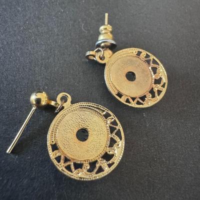 Gold-tone drop earrings featuring a black enameled central disc with a green shamrock or three-leaf clover design.
