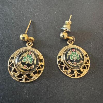 Gold-tone drop earrings featuring a black enameled central disc with a green shamrock or three-leaf clover design.