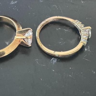 Two gold-toned rings, each featuring a prominent clear gemstone,