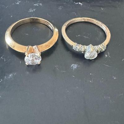 Two gold-toned rings, each featuring a prominent clear gemstone,