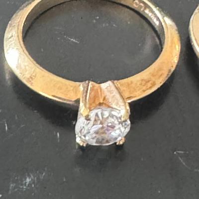 Two gold-toned rings, each featuring a prominent clear gemstone,