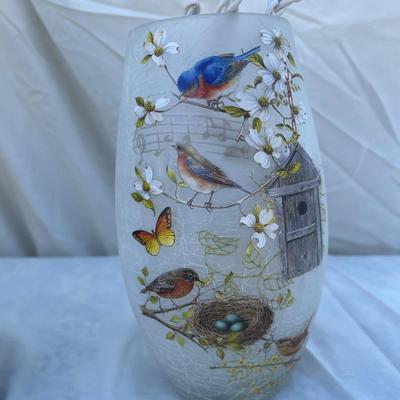 Sale Photo Thumbnail #85: Two decorative lamps, each approximately 8" tall. Left lantern is made of metal with glass sides, has a latched door and a ring on top for hanging, and has battery operated string lights and fake foliage inside. Right lamp is a glass vase with bird graphi