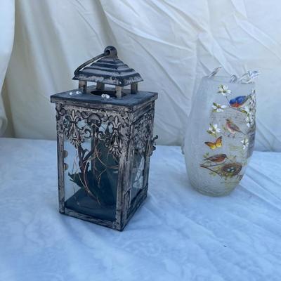 Sale Photo Thumbnail #84: Two decorative lamps, each approximately 8" tall. Left lantern is made of metal with glass sides, has a latched door and a ring on top for hanging, and has battery operated string lights and fake foliage inside. Right lamp is a glass vase with bird graphi