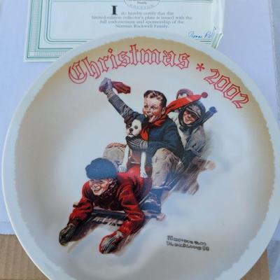 Sale Photo Thumbnail #205: This is a Norman Rockwell collector plate titled "The Christmas Sled," dated 2002. 
Artist:
Norman Rockwell, a renowned American painter known for his heartwarming depictions of American life. 
Theme:
Christmas, featuring a scene of children and a dog sle