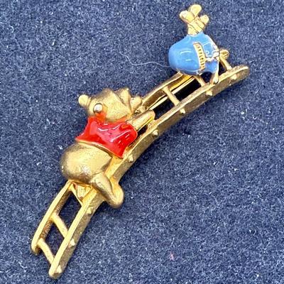 Sale Photo Thumbnail #462: This is a brooch/pin has Pooh climbing a ladder to reach a pot of honey. .It measures 1 inches  high x 2.5 inches wide. Very good condition.