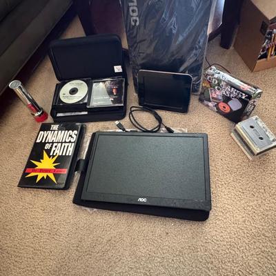 AOC portable monitor, The Dynamics of Faith" book by Peter Lowe, and a CD/DVD case with various discs.