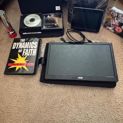 AOC portable monitor, The Dynamics of Faith" book by Peter Lowe, and a CD/DVD case with various discs.