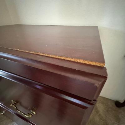 Wooden, two-drawer filing cabinet with brass-toned handles and a key in the top drawer's lock.