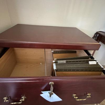 Wooden, two-drawer filing cabinet with brass-toned handles and a key in the top drawer's lock.