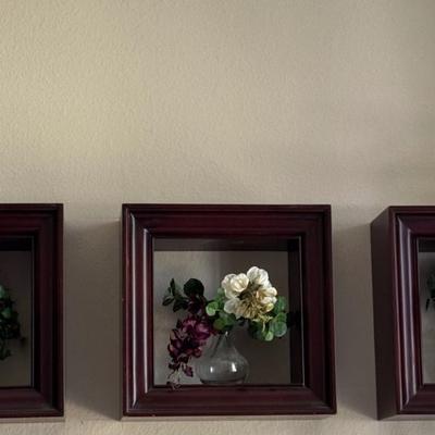 Three shadow boxes, a type of framed wall decor, each containing an arrangement of artificial flowers.