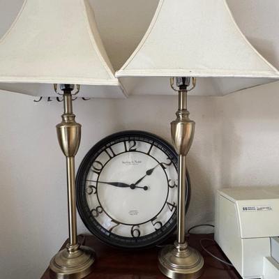 Pair of classic-style table lamps with cream-colored bell lamp shades and a large round wall clock with a dark frame and white face.