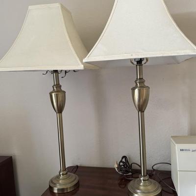 Pair of classic-style table lamps with cream-colored bell lamp shades and a large round wall clock with a dark frame and white face.