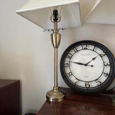 Pair of classic-style table lamps with cream-colored bell lamp shades and a large round wall clock with a dark frame and white face.
