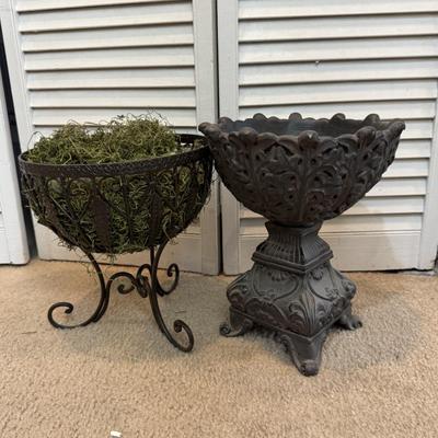 Two ornate, dark-colored decorative containers, commonly identified as planters or urns, likely made of cast iron.