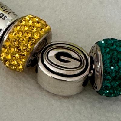 Sale Photo Thumbnail #70: Chamilia Charm Bracelet with various charms. These include Green Bay Packers-themed charms and an inspirational charm with the words "the things I cannot". The bracelet is displayed in a round, lime green Chamilia box. 
Here's more about the product:
Cham