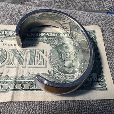 Sale Photo Thumbnail #505: bangle bracelet featuring shell inlay, likely crafted with mother-of-pearl or abalone shell set into a metal base. 
Key details about this item:
Type: It's a bangle bracelet, characterized by its rigid, non-flexible circular form that slips over the hand 
